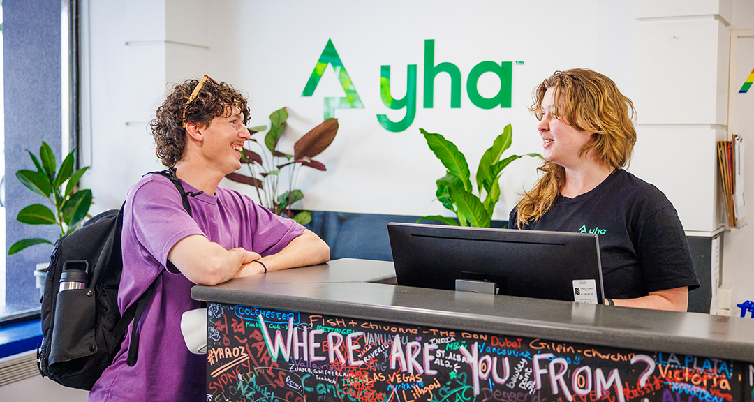 Pogovor med gostoma in osebjem na recepciji YHA hostla.